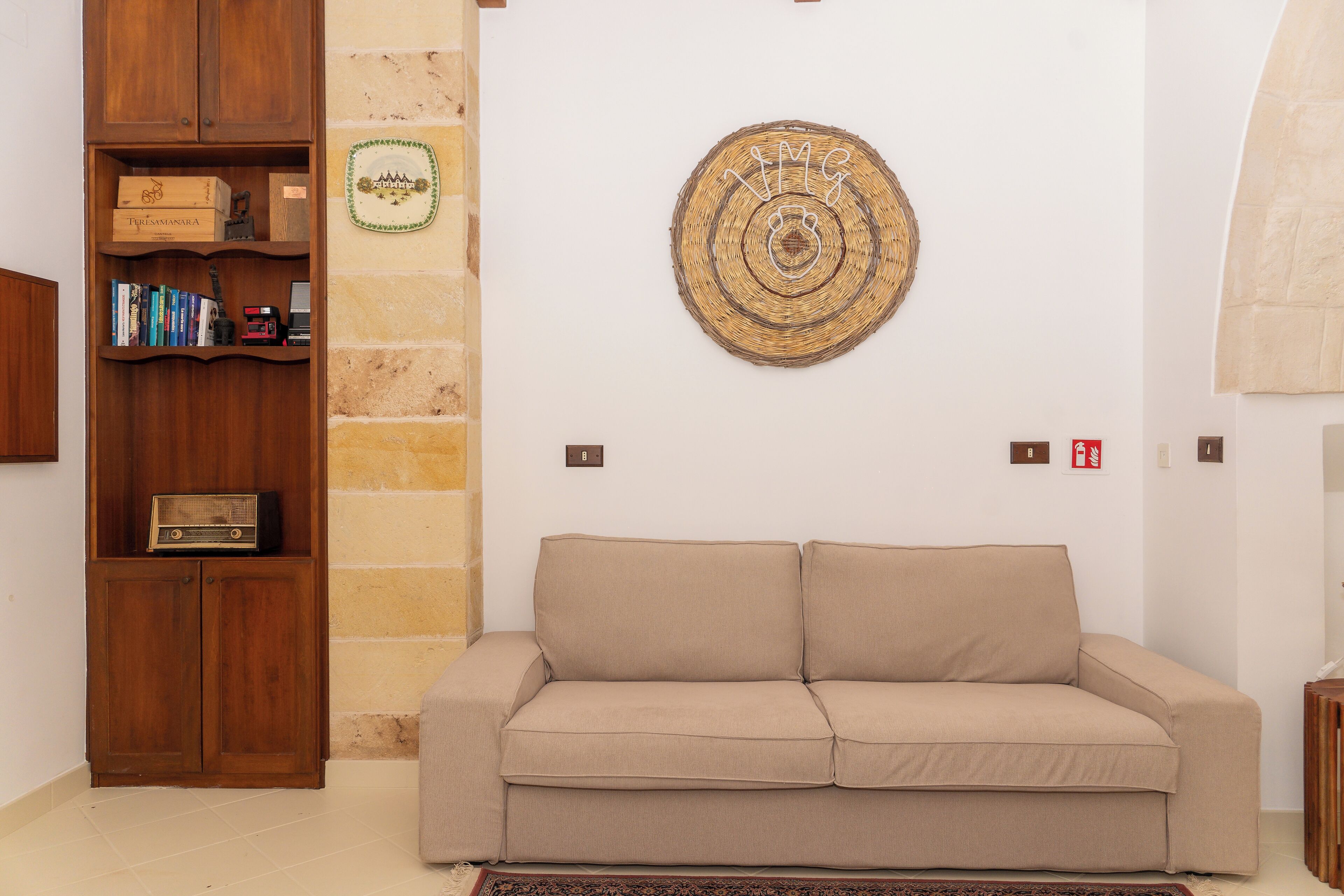 Un salón con un sofá beige, una estantería de madera y un tapiz decorativo.