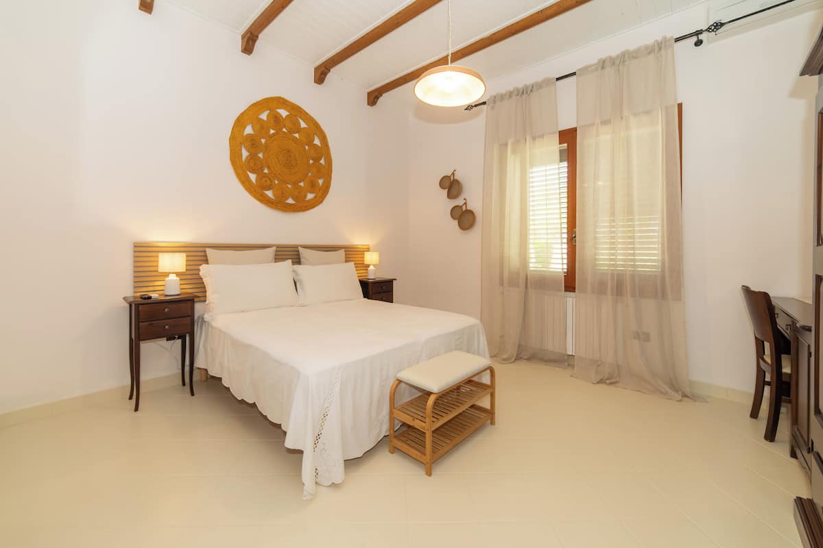 A bedroom with a large bed, bedside tables, a wooden bench, and a ceiling fan.
