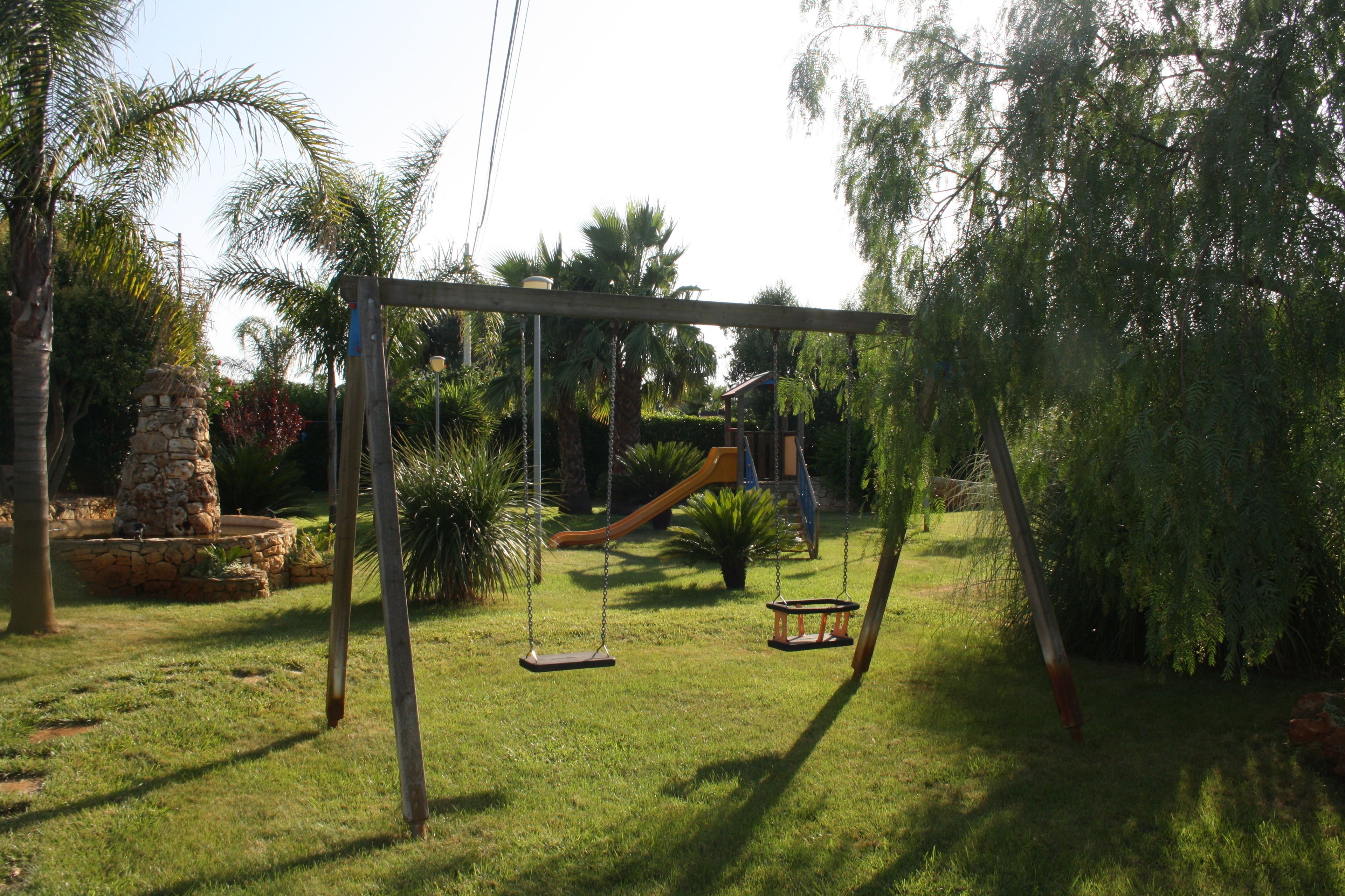 A swing set in a grassy area with a stone structure and a slide in the background.