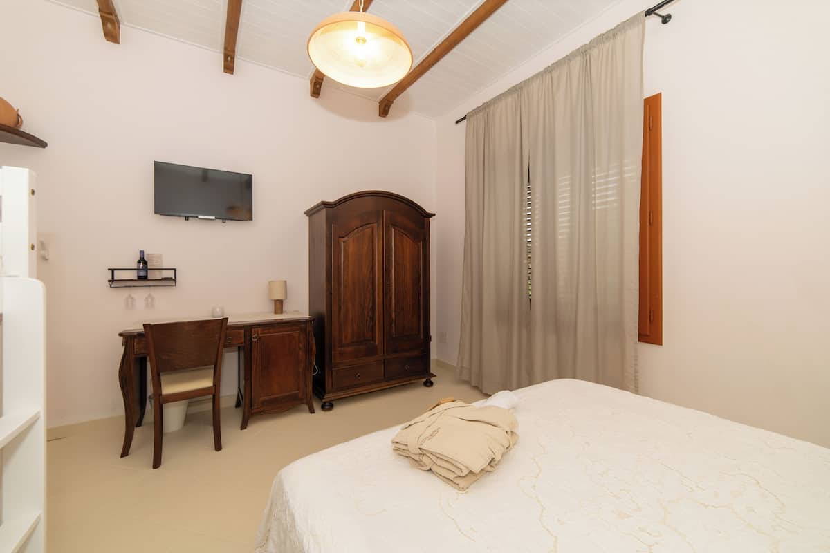 A bedroom with a bed, a desk, a wardrobe, a television, and a window with curtains.