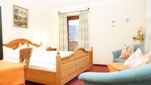 Habitación de hotel con una cama de madera, un sofá azul, una mesita pequeña y una ventana con cortinas.