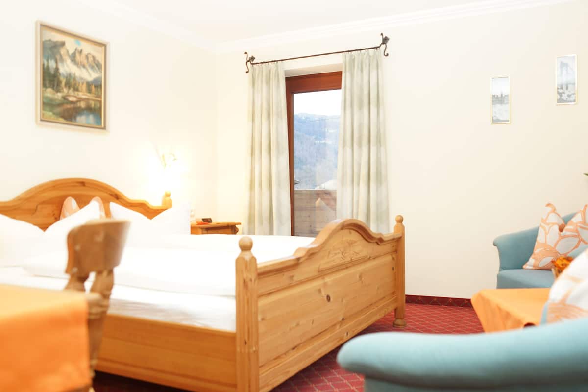 A hotel room with a wooden bed, a blue sofa, a small table, and a window with curtains.