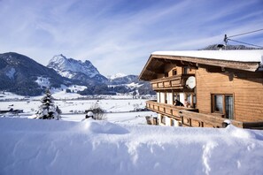 Een houten chalet met een balkon met uitzicht op een besneeerd landschap en bergen.