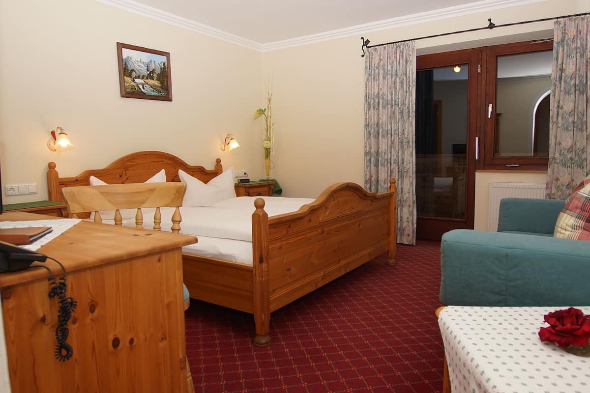 A bedroom with a wooden bed, a desk, a chair, and a window with curtains.