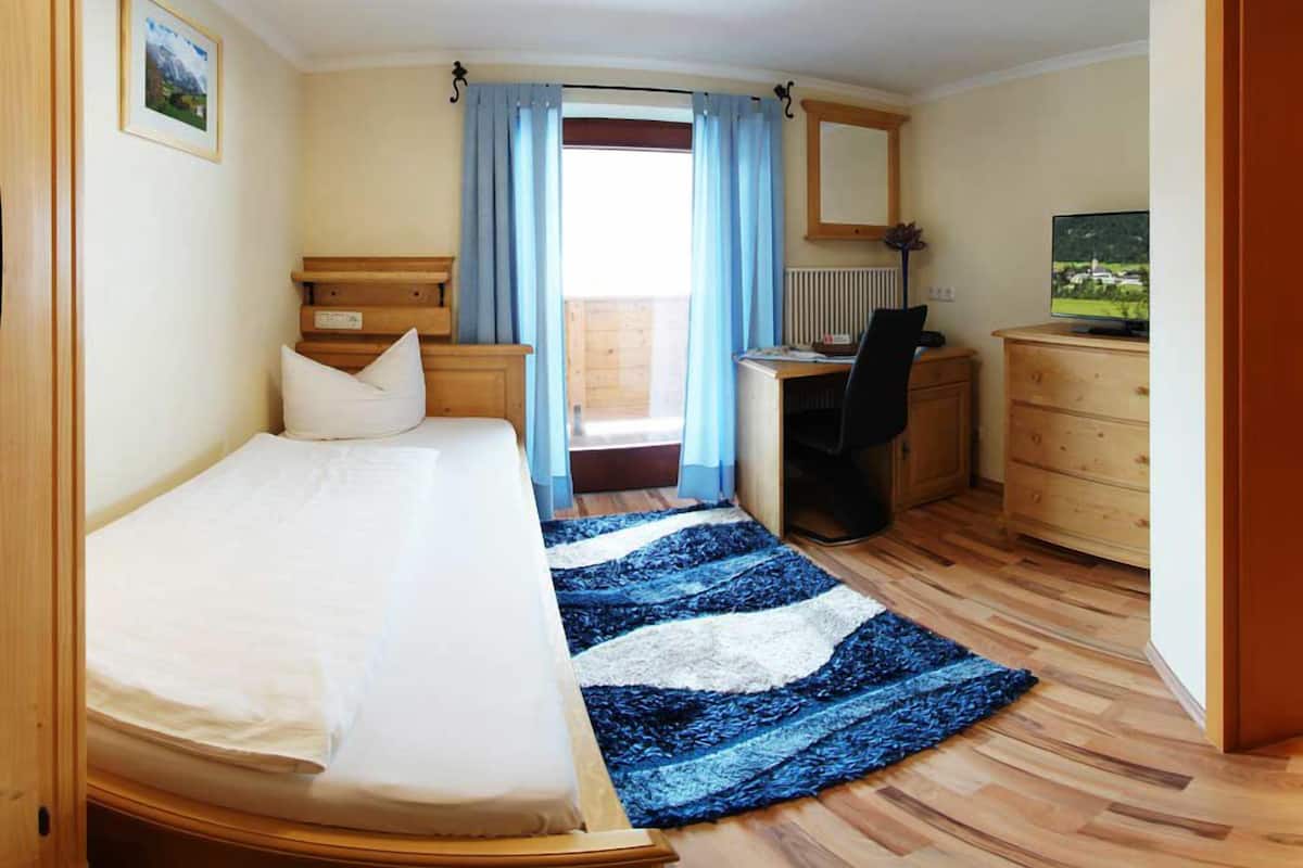 A hotel room with a bed, desk, chair, dresser, and a view of the outdoors.