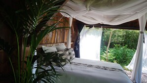 Un dormitorio con cama, cortinas blancas y vista a la vegetación.