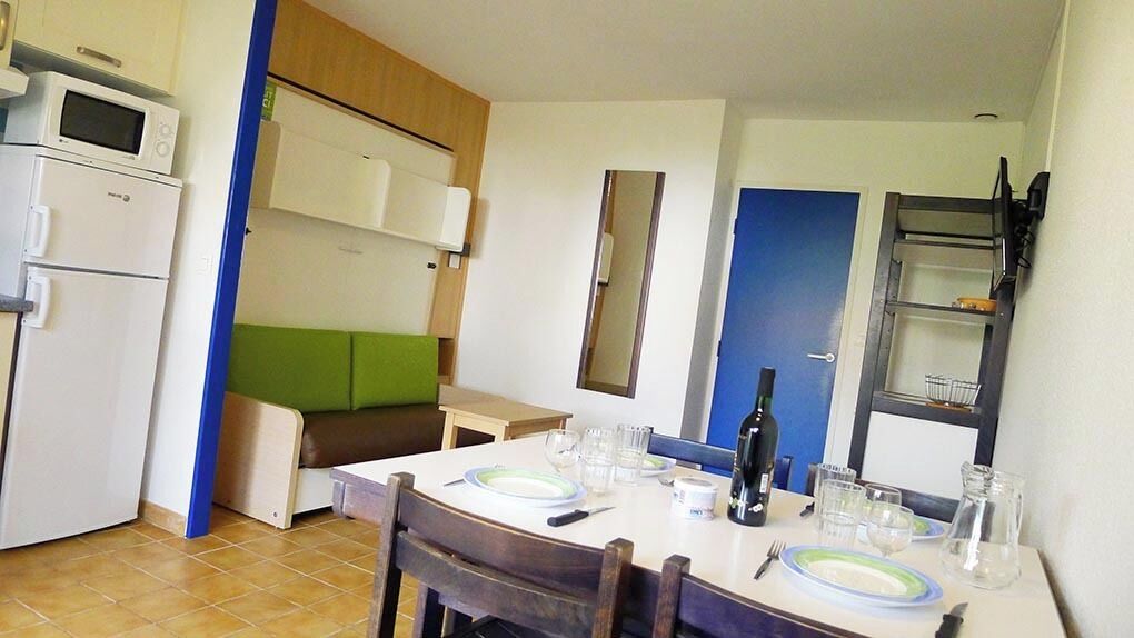 Cocina compacta con comedor, microondas, refrigerador y una puerta azul.