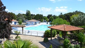 A swimming pool with lounge chairs and a pavilion, surrounded by greenery and a clear sky.
