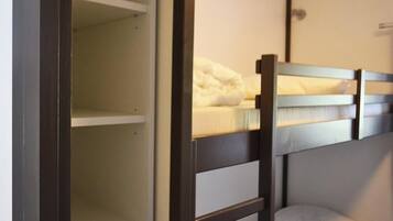 Un lit superposé avec un matelas et des oreillers blancs, une tête de lit en bois et un mur blanc avec un interrupteur.
