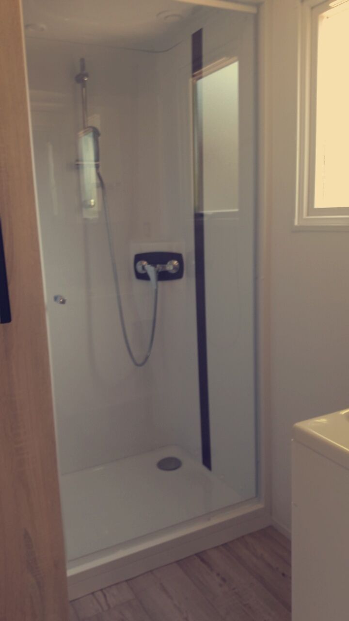 Een douchecabine met glazen wanden, een handdouche en bedieningspaneel.