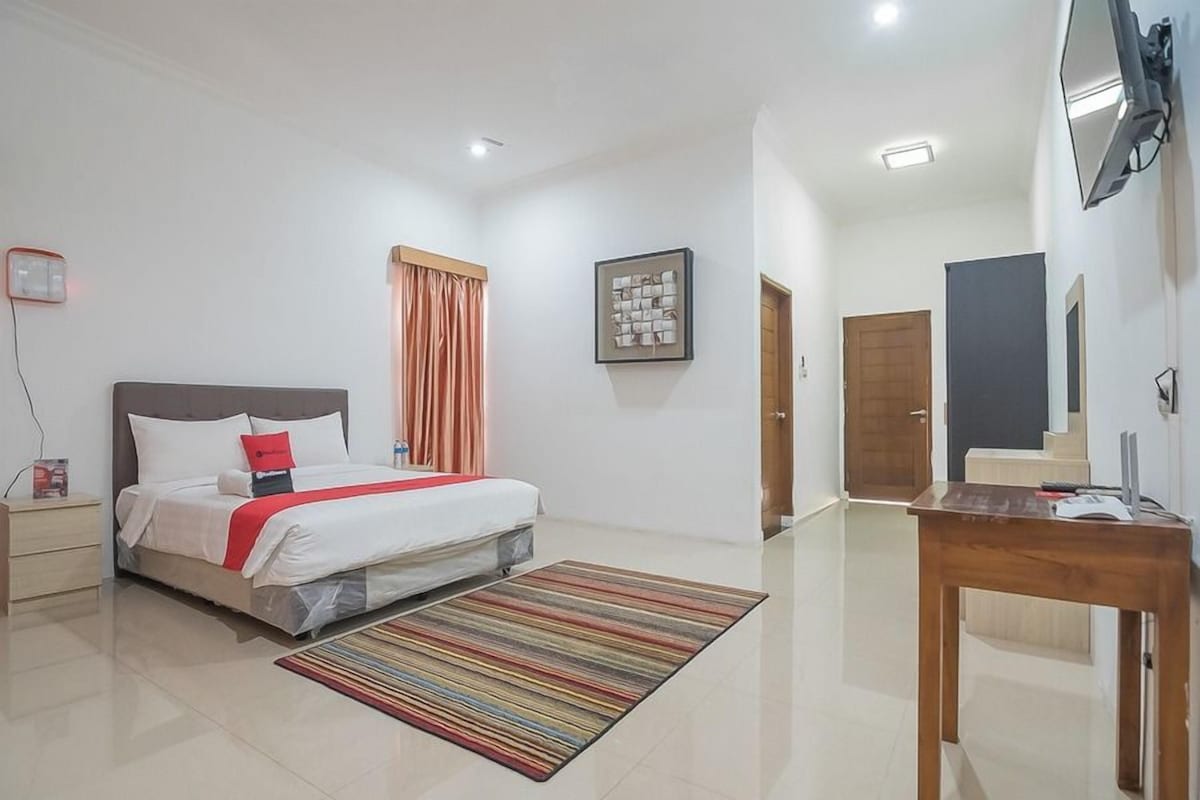 A hotel room with a bed, a bedside table, a desk, a chair, a TV, and a door.