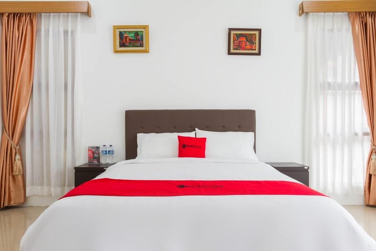 A hotel room with a bed, a nightstand, two framed pictures, and curtains.