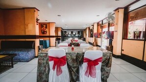 Un comedor con una mesa larga, sillas blancas con cintas rojas y un mantel estampado.
