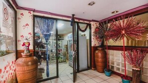 Una tienda con entrada de puerta de vidrio, piso de baldosas y diversos objetos decorativos, incluyendo jarrones grandes y plantas en macetas.