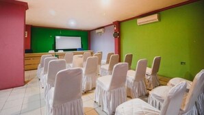 Un salón de conferencias con filas de sillas cubiertas de blanco, una pantalla verde y un equipo de aire acondicionado.