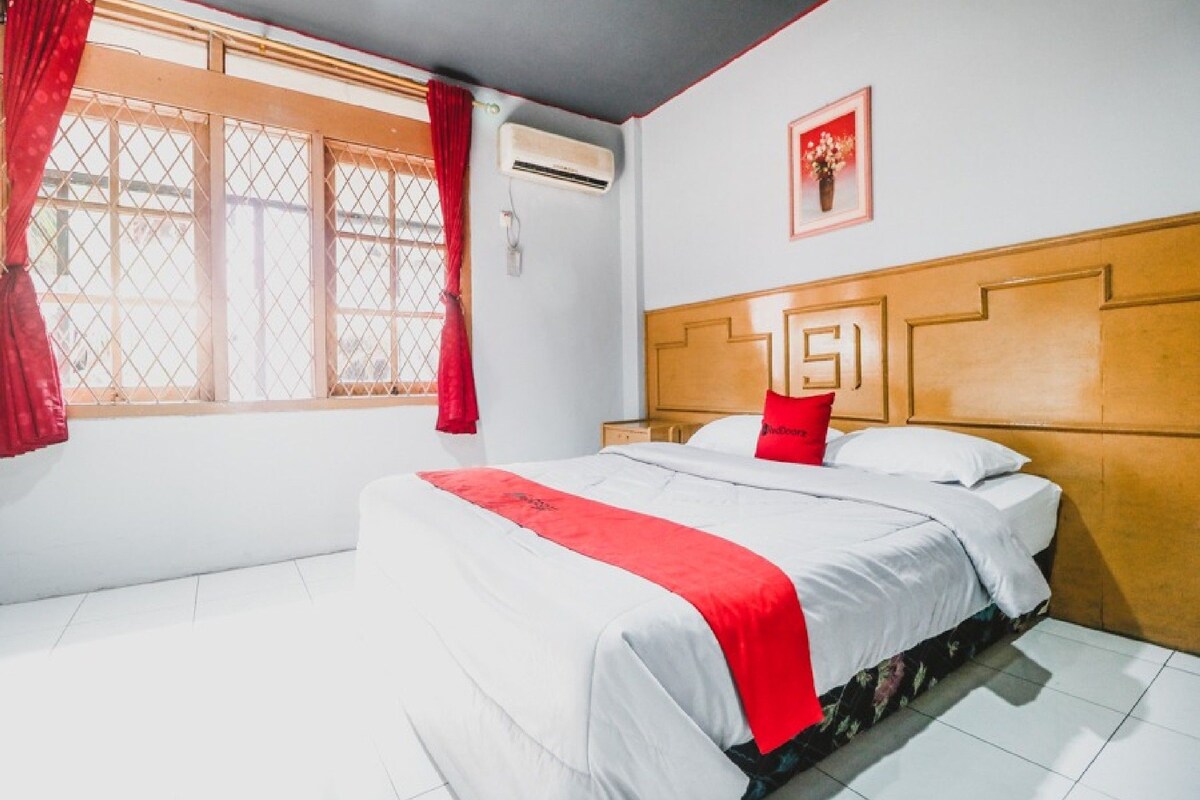 Une chambre d’hôtel avec un lit, une fenêtre avec des rideaux, un appareil de climatisation et un tableau encadré au mur.