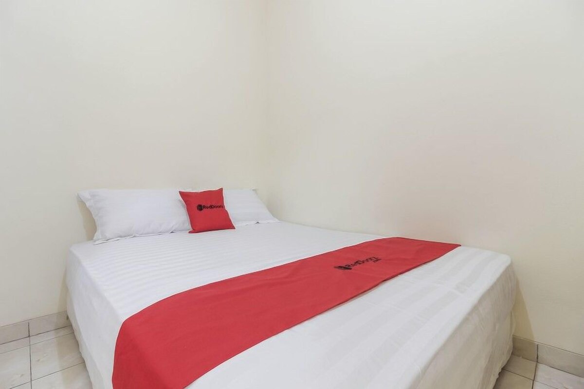 Een enkel bed met een witte matras en rode beddengoed, inclusief een rode plaid en kussen met een logo.