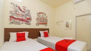 Een hotelkamer met twee bedden, elk voorzien van een rode en witte spreidek en kussens, en een muurschildering van een stadsgezicht.
