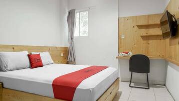 A bedroom with a wooden bed, a desk with a chair, a TV mounted on the wall, and a window with curtains.