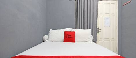 A hotel room with a bed, a red and white bedspread, a red pillow, a grey curtain, and a white door.