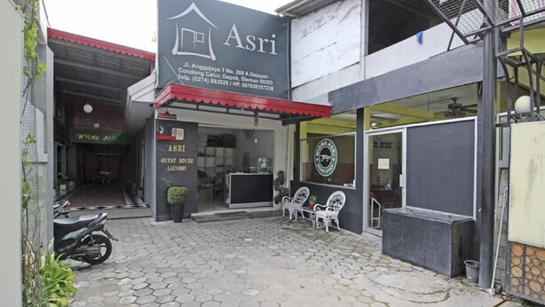 A guest house named Asri with a red awning, a motorcycle parked outside, and a paved courtyard. - RedDoorz near Terminal Condong Catur (Depok)