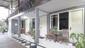 A covered outdoor seating area with chairs and tables, a checkered floor, and a motorcycle parked outside. - RedDoorz near Terminal Condong Catur (Depok)