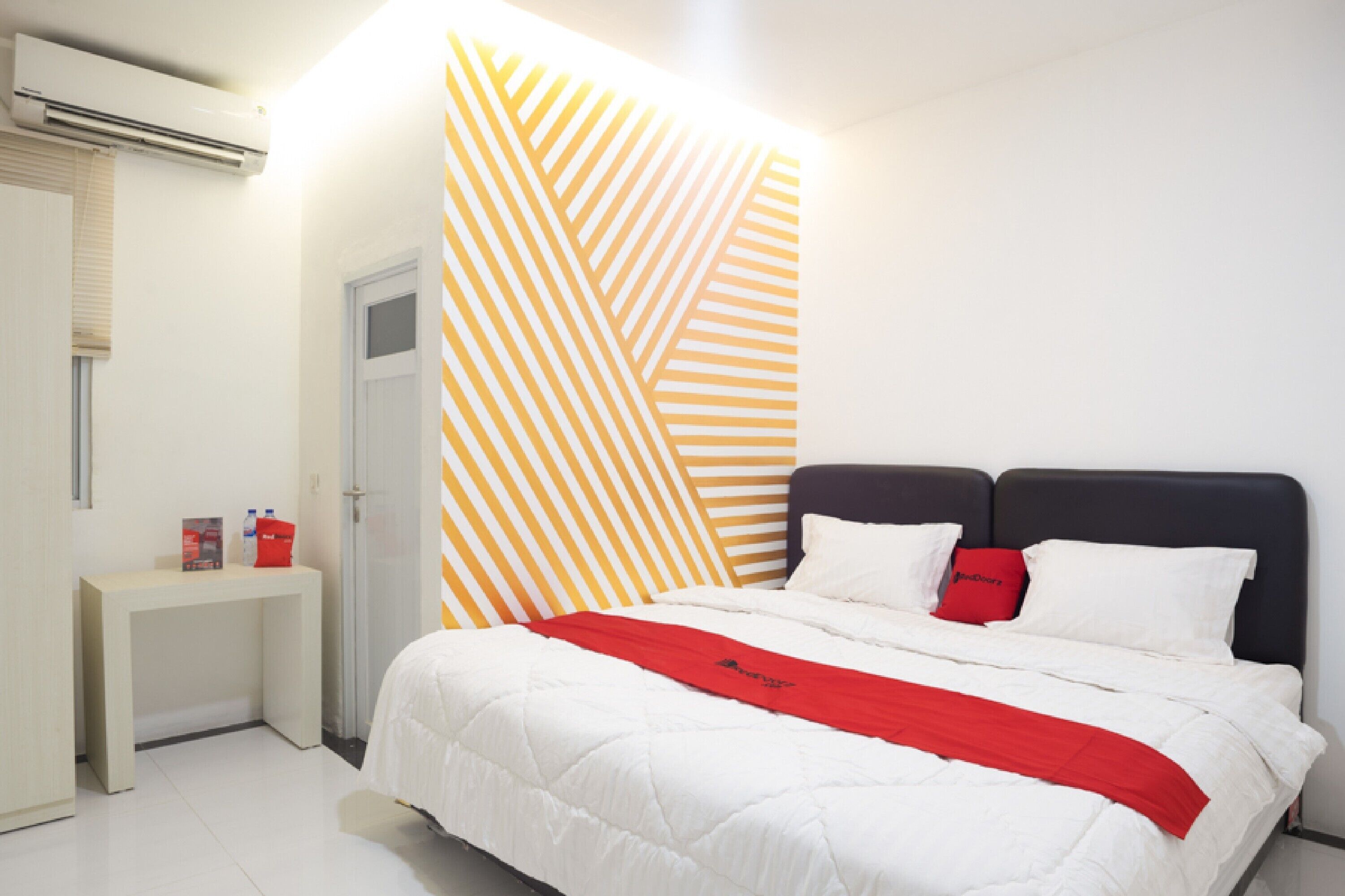 Une chambre d’hôtel avec un lit, une table de chevet, un oreiller rouge et un mur orné d’un motif géométrique.