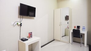 Habitación de hotel con televisor de pantalla plana montado en la pared, escritorio con silla, armario y una mesita con teléfono y folleto.