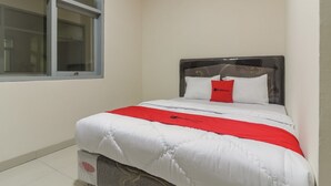 A neatly made bed with a white and red bedspread, a dark headboard, and a window with blinds.