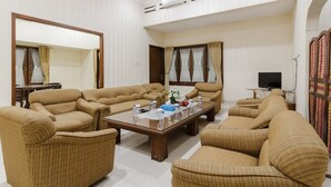 A spacious living room with beige sofas, a glass coffee table, and a television.