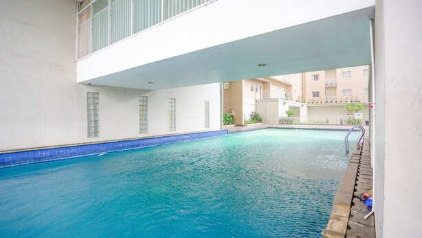 An indoor swimming pool with clear blue water, a tiled edge, and a balcony overlooking the pool area. - RedDoorz Apartment @ Bogor Valley (Bogor)