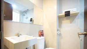 A bathroom with a white sink, toilet, and shower. There is a mirror above the sink and a shelf with towels above the toilet. - RedDoorz Apartment @ Bogor Valley (Bogor)