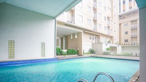A swimming pool with a clear blue water, surrounded by a white building with balconies and windows. - RedDoorz Apartment @ Bogor Valley (Bogor)