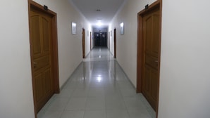 A long, narrow hallway with wooden doors on both sides and a tiled floor. - RedDoorz Plus near WTC Batanghari Mall (Jambi)