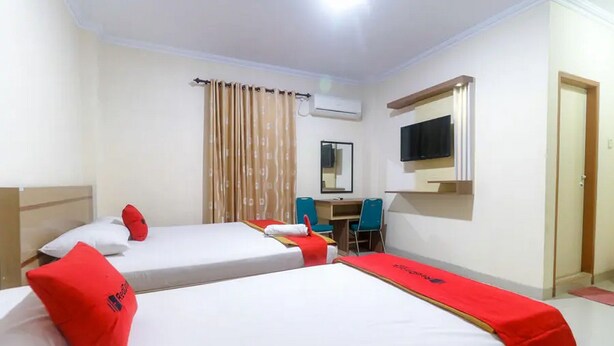 A hotel room with two beds, a desk, a chair, a TV, and an air conditioning unit. - RedDoorz Plus near WTC Batanghari Mall (Jambi)