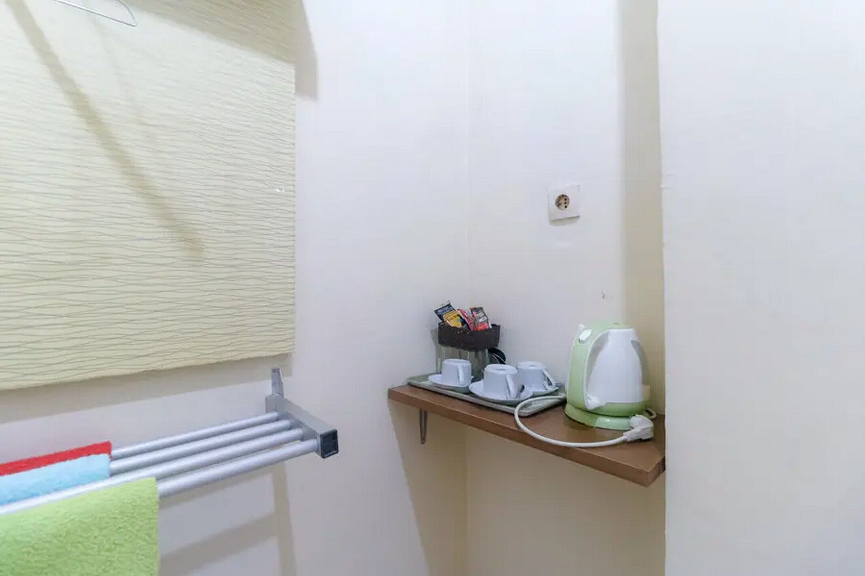Un baño pequeño con un perchero, una repisa con una tetera y tazas, y una ventana con persianas.