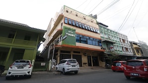 A multi-story building with a sign for 'Hotel Pinang' on the ground floor. There are parked cars in front of the building. - RedDoorz Plus near WTC Batanghari Mall (Jambi)