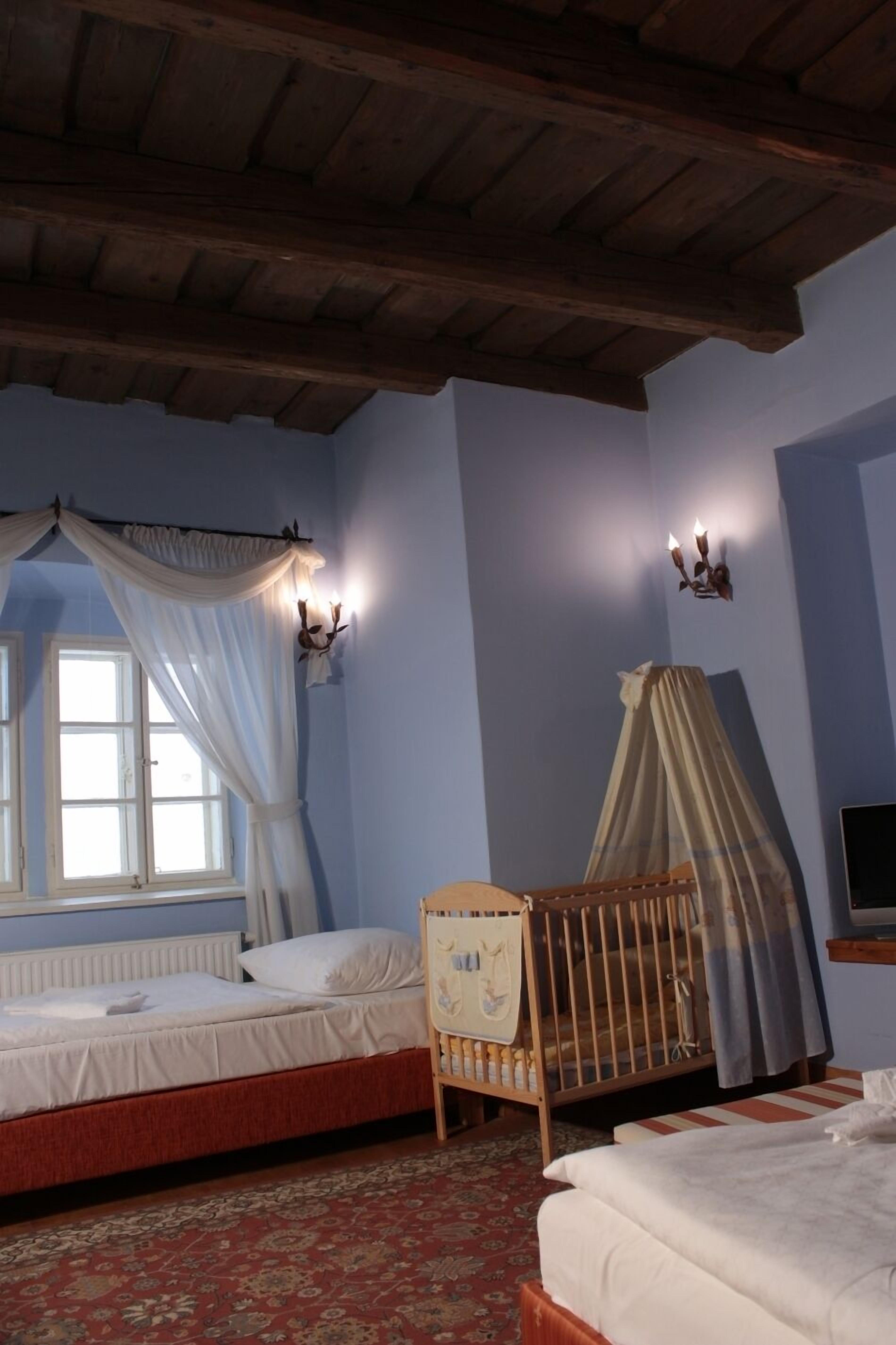 A room with a wooden ceiling, a bed with a canopy, a crib, and a window with curtains.