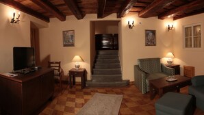 A cozy living room with a wooden staircase, a television, and two lamps. - Penzión Cosmopolitan II. (Banska Stiavnica)