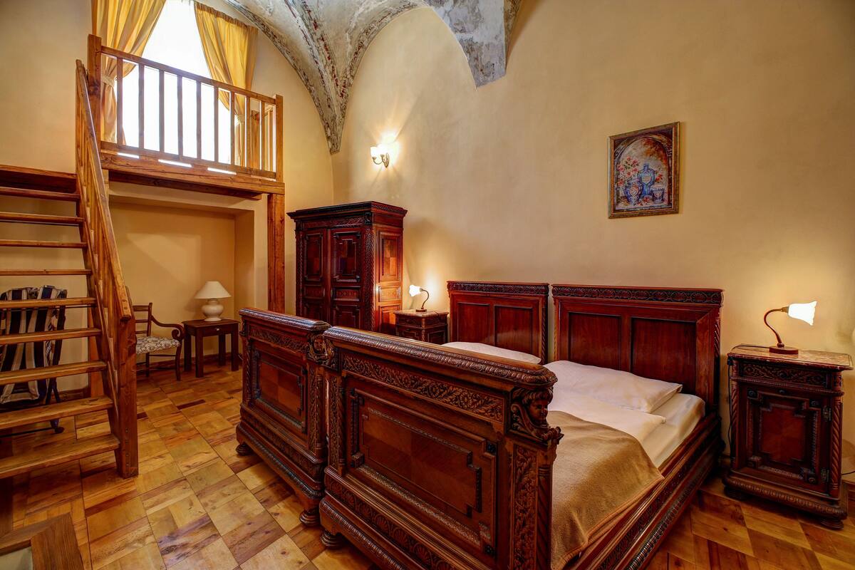 A traditional bedroom with a wooden four-poster bed, a wooden ladder, a desk, and a chair.