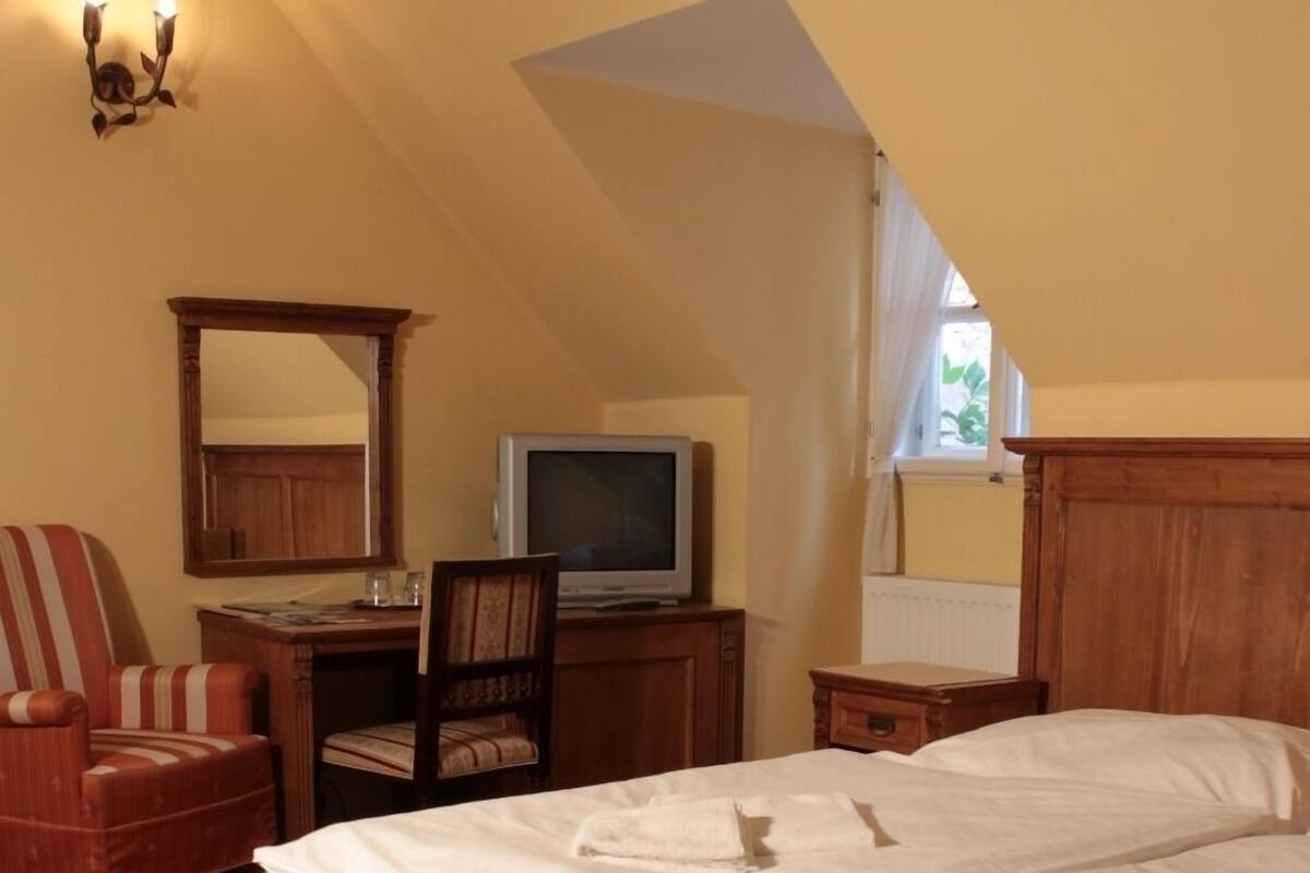 A bedroom with a large bed, a desk with a computer, a chair, and a television.