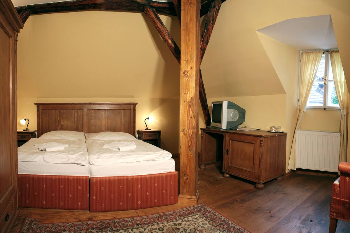 A bedroom with a double bed, wooden furniture, a television, and a window with curtains.