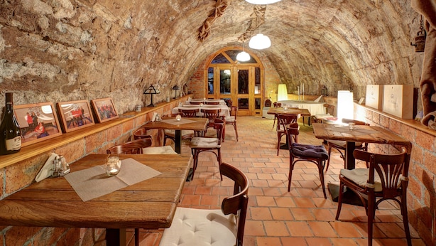 An underground dining area with rustic brick walls, wooden tables, and chairs. - Penzión Cosmopolitan II. (Banska Stiavnica)