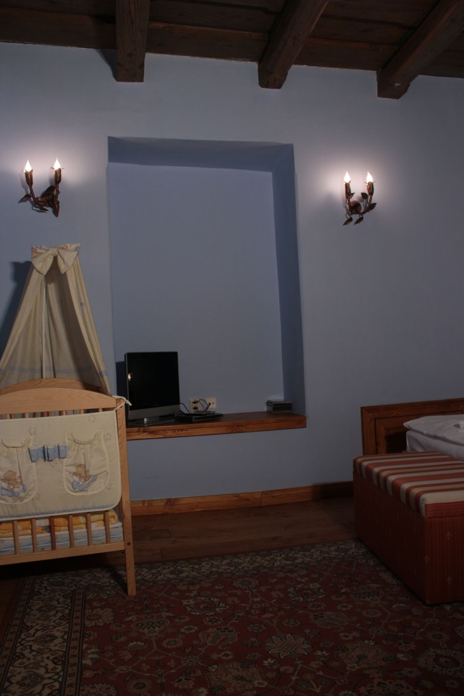 A bedroom with a wooden crib, a small bedside table with a television, and a bed with a striped bedspread.