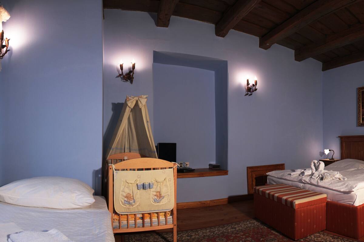 A bedroom with a wooden bed, a bedside table, a nightstand, a window with curtains, and a wall-mounted lamp.