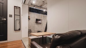 Ein modernes Zimmer mit einer Ledersofa, einem Holztisch, einem an einer strukturierten Wand montierten Fernseher und einer Tür mit Griff.