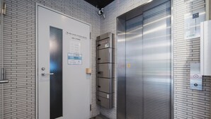 Ein Aufzug mit Metalloptik, eine Tür mit Glasfenster und ein Schild mit dem Hotelnamen und den Check-in-Zeiten.