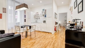 A modern kitchen with white cabinets, a dining area with a table and chairs, and a living area with a black TV stand. - Residenza Le Gemelle di Roma (Rome)