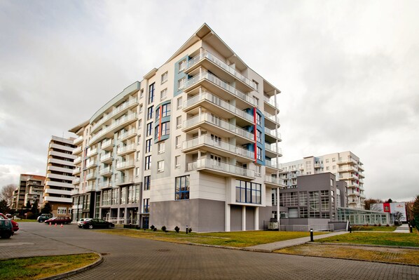 Ein mehrgeschossiges Wohngebäude mit Balkonen, einem Parkplatz und einem kleinen Garten.
