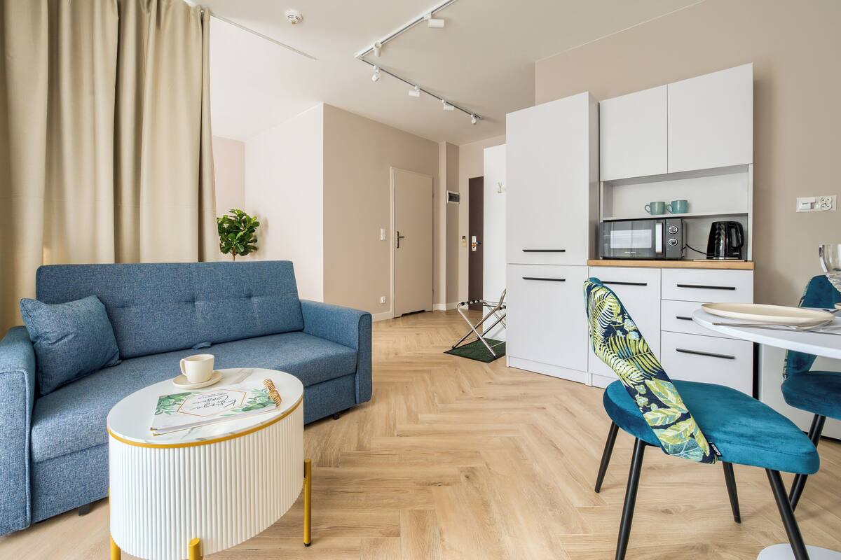 Una sala de estar moderna con un sofá, una mesita redonda y una cocina con armarios y un microondas.